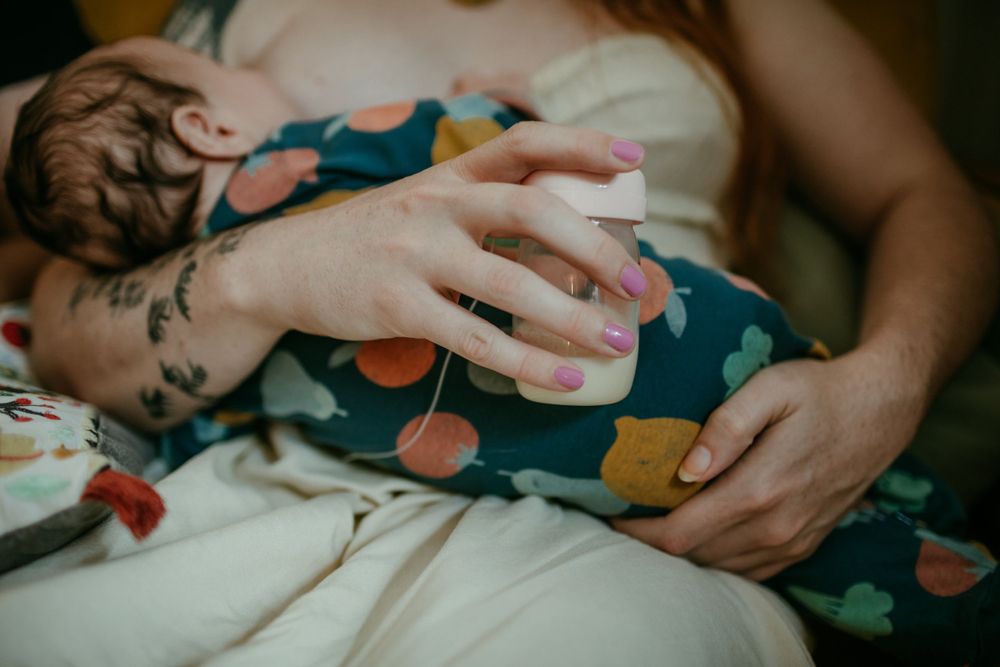 close up of parent chestfeeding infant while holding milk in bottle portland oregon in home newborn photographer