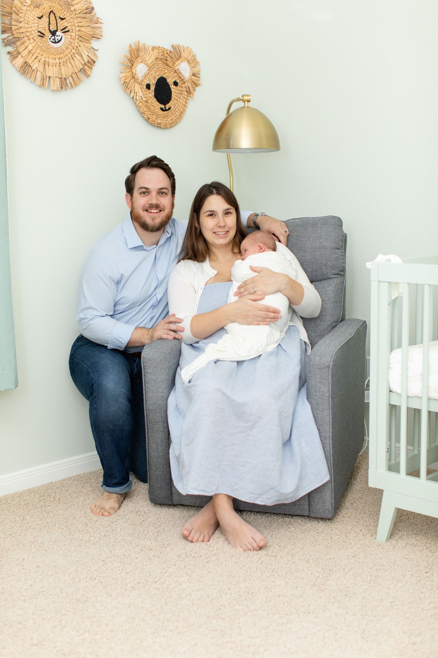 Family poses together in nursery with koala wall decor and gold lamp.