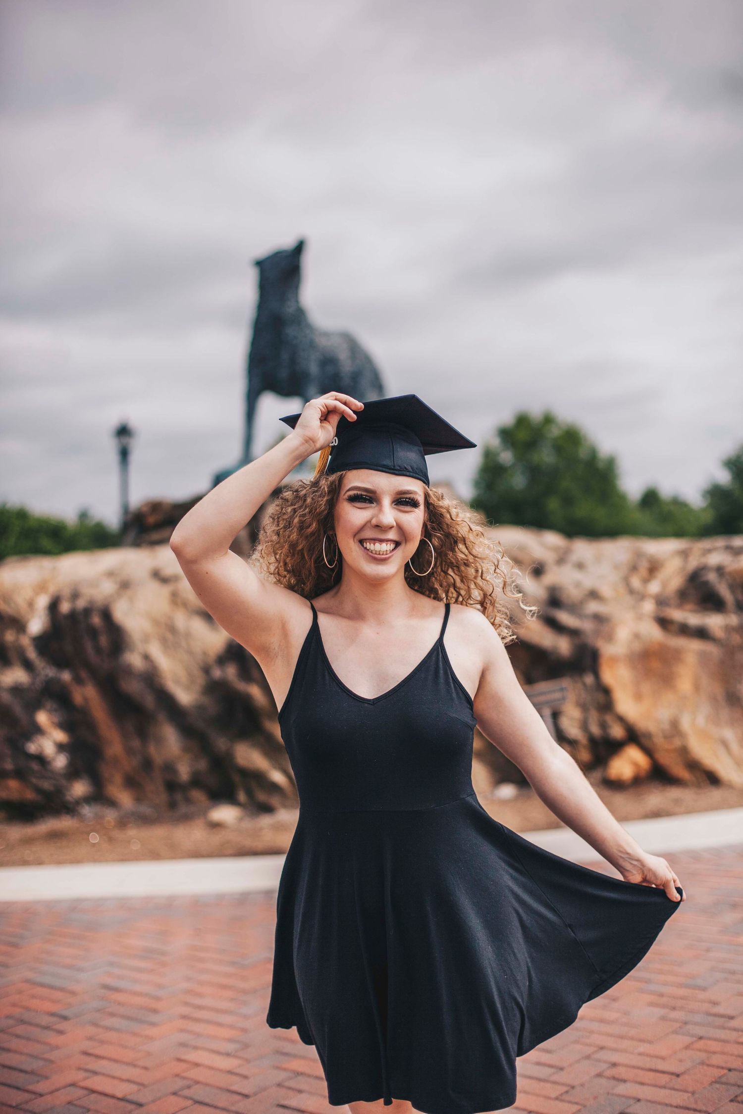 Smiling female graduate in black dress twirls near University of West Georgia wolf statue.