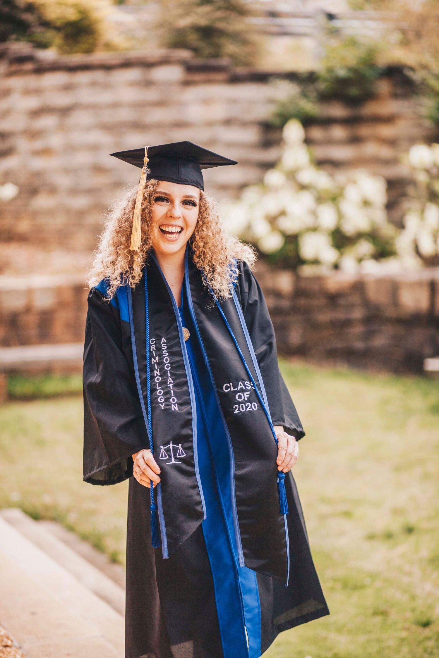 Female graduate in black cap and gown with Class of 2020 blue stole.