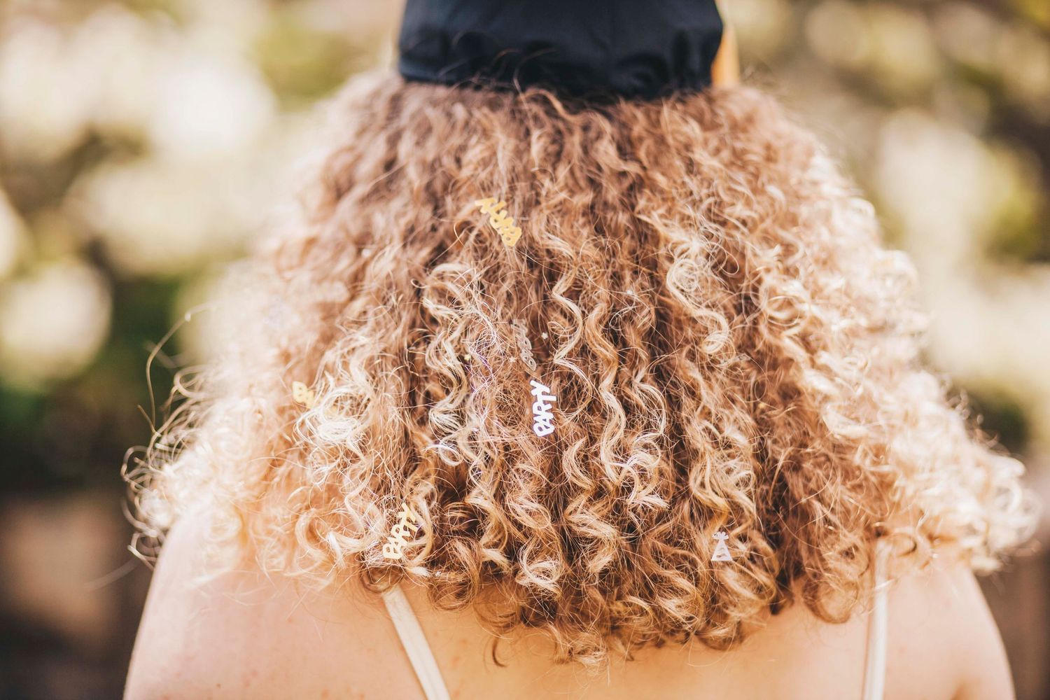 Close-up back view of a woman with beautiful curly blonde hair wearing a black graduation cap.