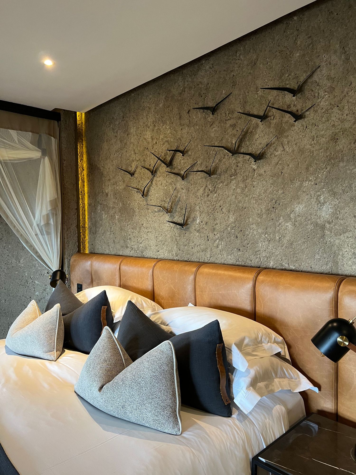 Contemporary bedroom with leather headboard and metal bird wall art featuring neutral toned pillows.