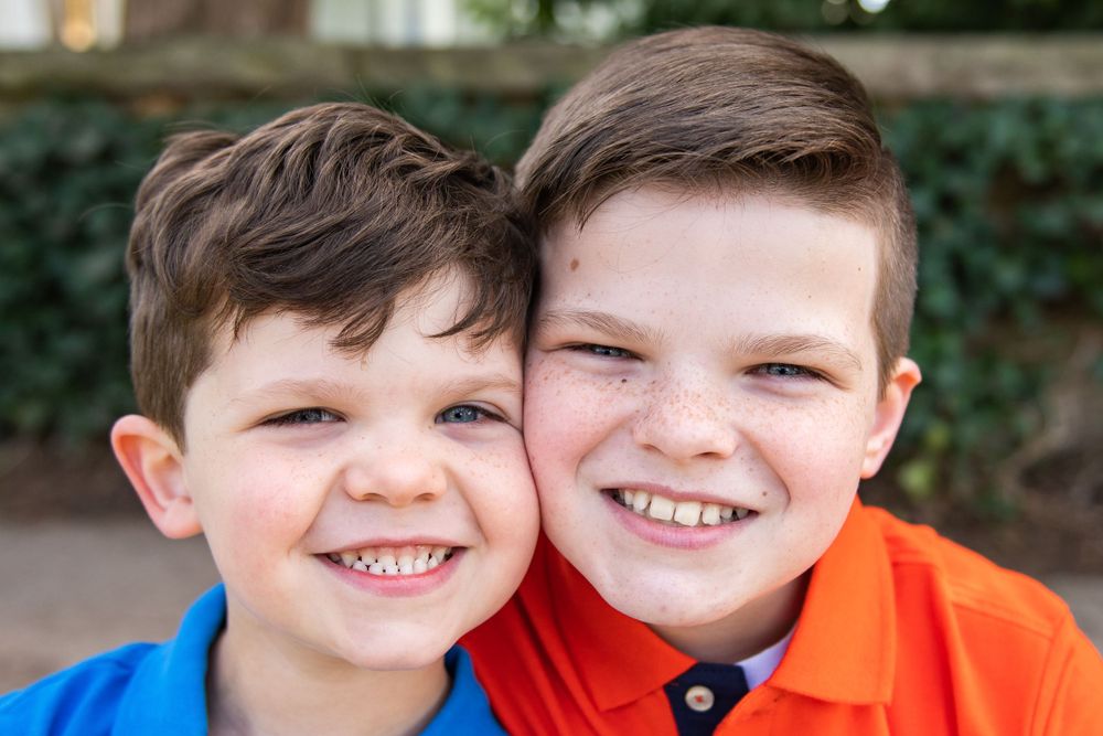 Two children in bright shirts smile together during outdoor photo session.