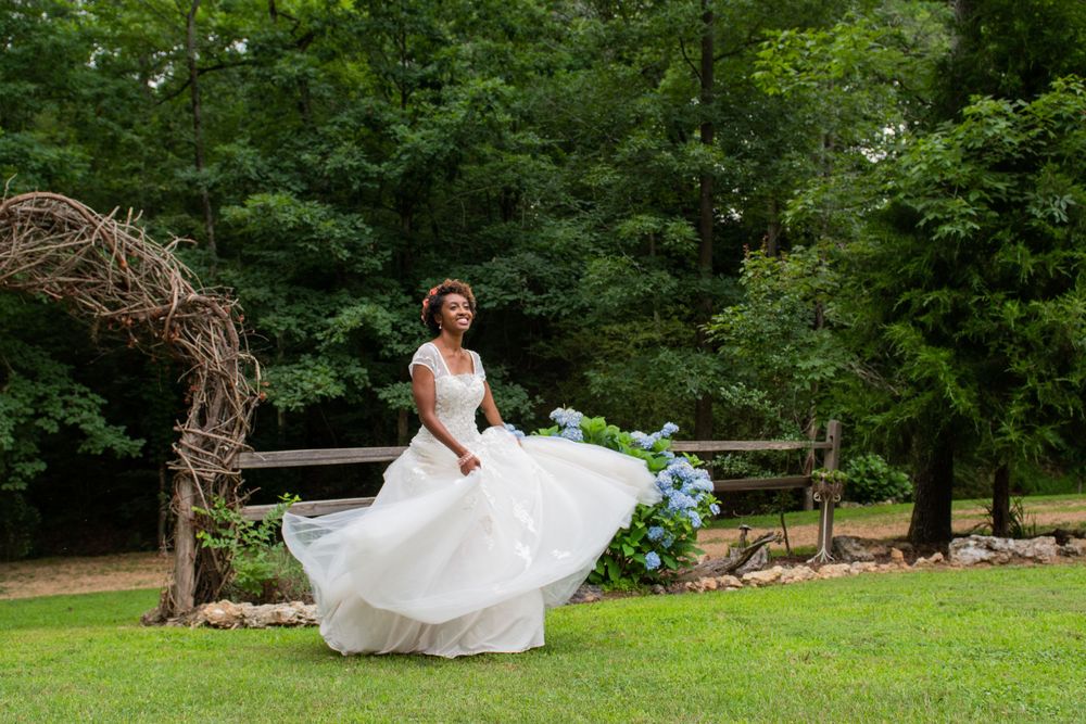 White wedding dress twirls elegantly across a lush green lawn in a wooded setting.