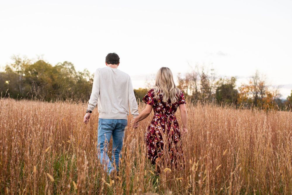 Couple walks through a golden field of tall grass during sunset.