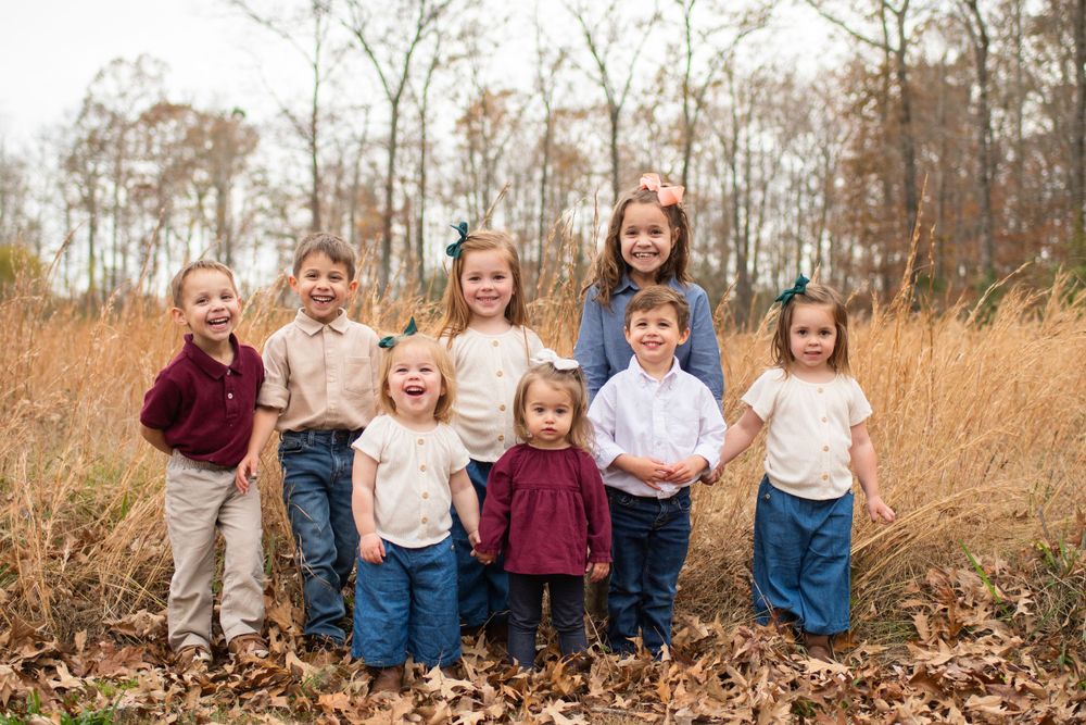 Family group poses together among fallen autumn leaves in natural outdoor setting.