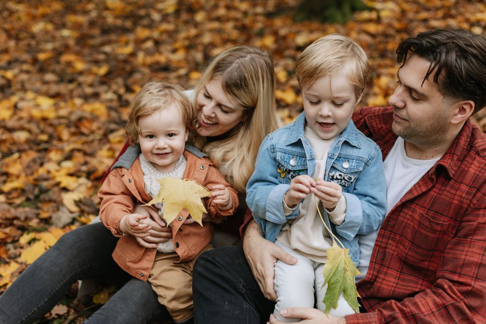 Family sitting together on fallen autumn leaves during an outdoor photoshoot.