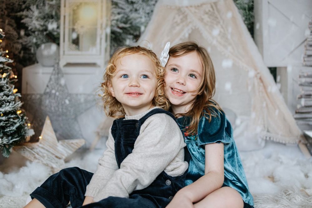 Two children sit together in front of a teepee tent with winter decorations.