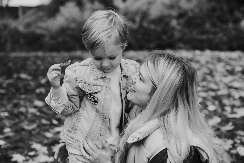 Black and white portrait of tender moment between parent and child among fallen leaves.