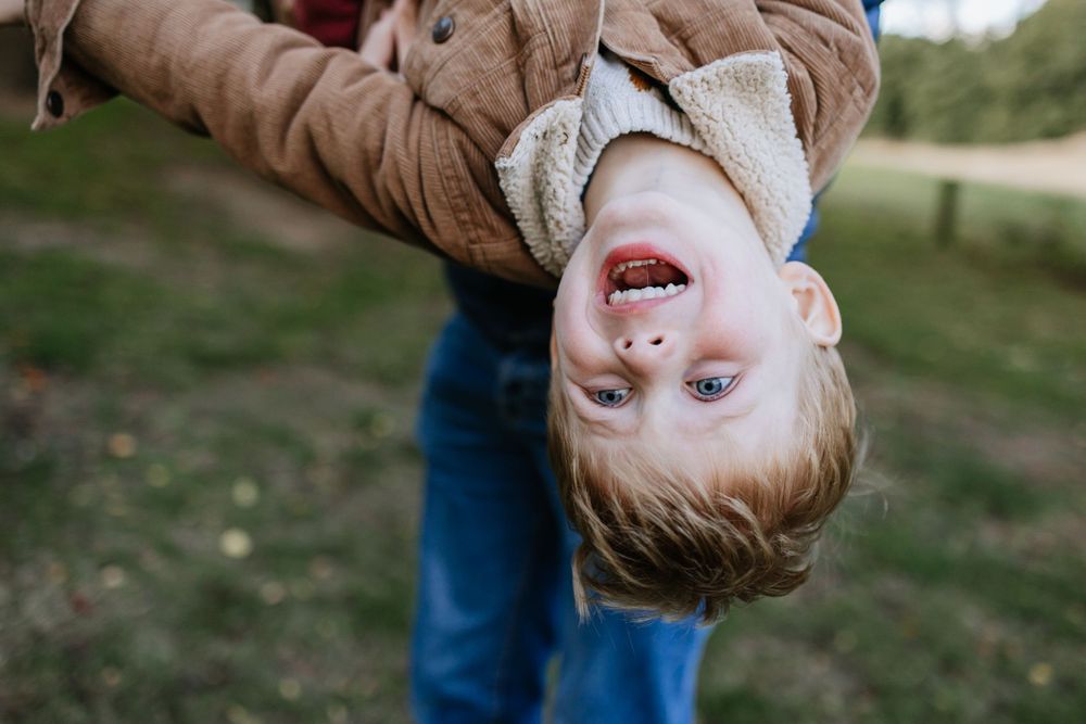 Playful upside-down portrait of a child being held in the air outdoors.