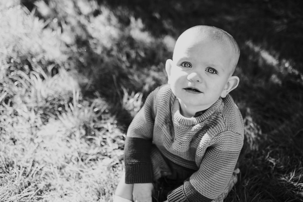 Black and white portrait of a small child sitting outdoors in natural lighting.