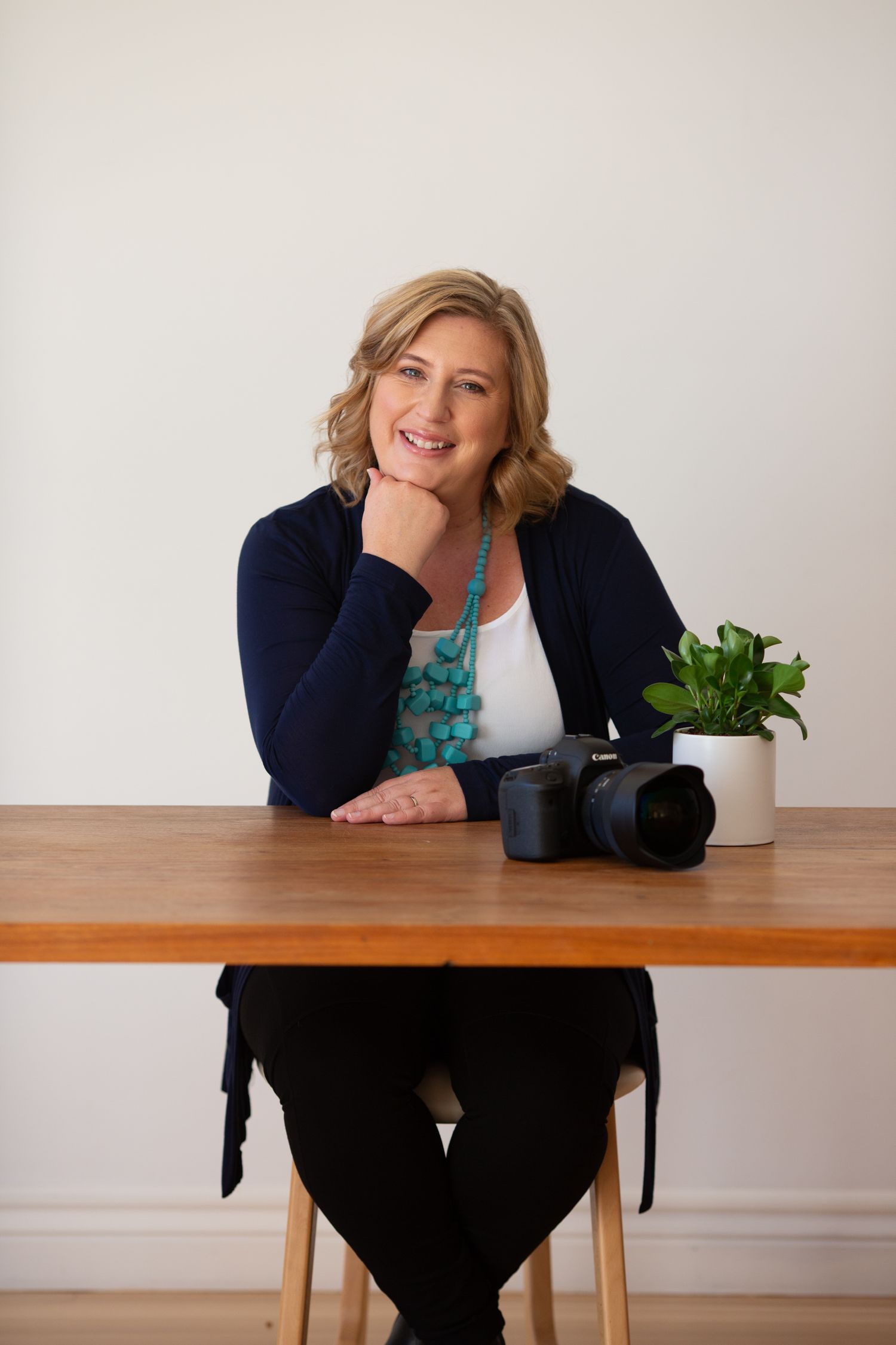 Photographer seated at wooden desk with camera and plant displaying casual professional style.