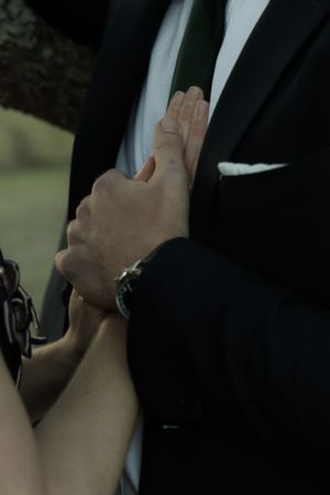 Hands gently adjusting the lapel of a black formal suit.