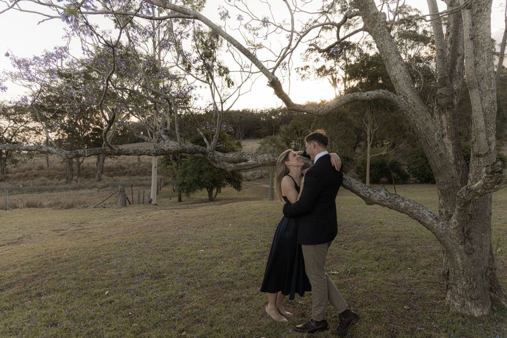 Couple in formal attire sharing a tender moment under trees at sunset.