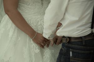 Close-up shot of couple's hands clasped together, showing wedding attire details.