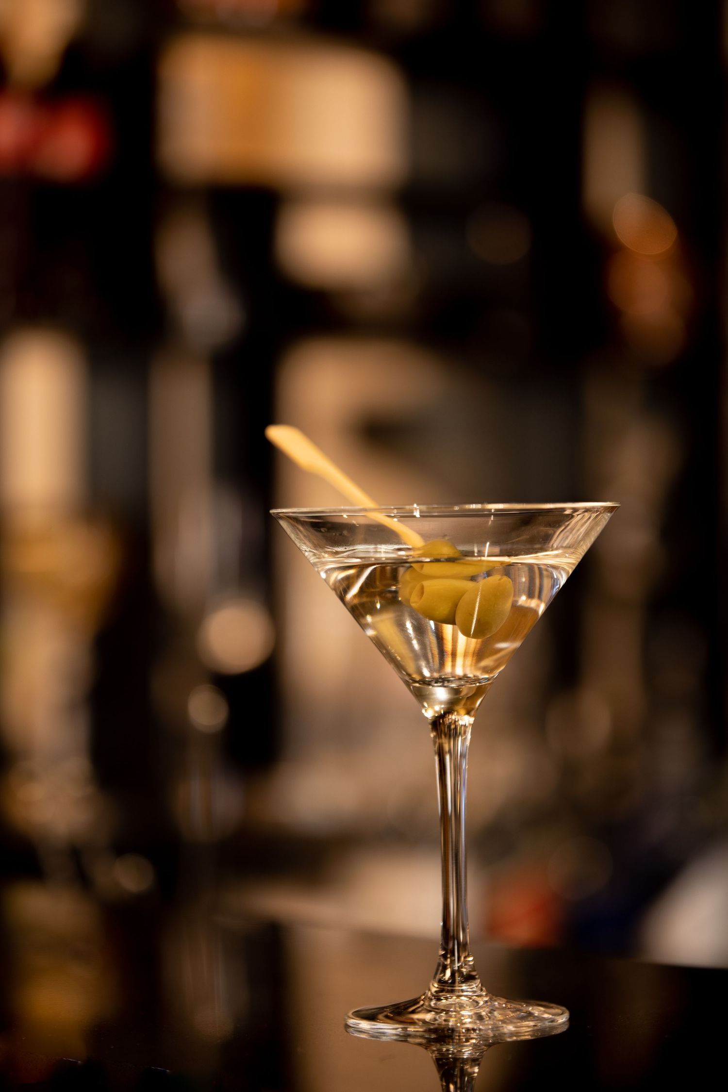 Close-up of classic martini cocktail with olive garnish in stemmed glass against dark background.