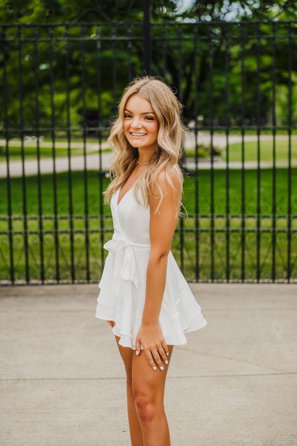 Summer fashion photoshoot in front of a black iron fence with green landscaping.