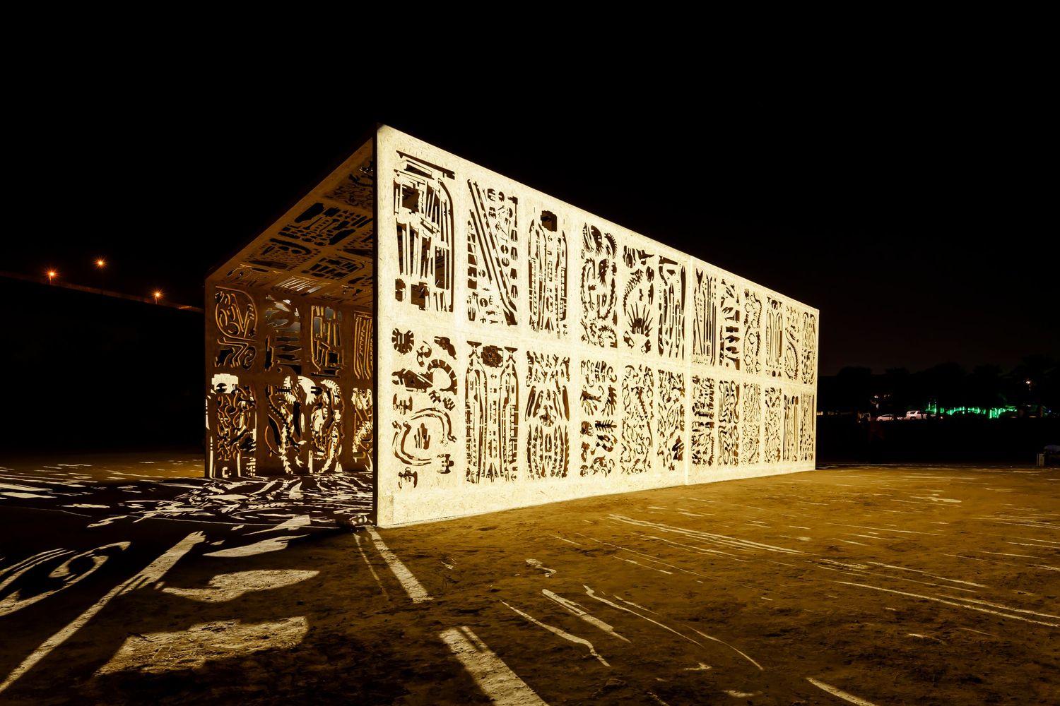 Illuminated architectural structure with intricate cutout patterns glowing at night.