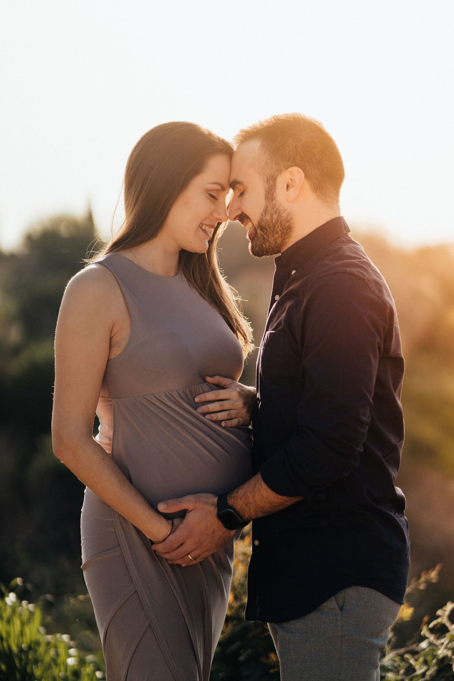 Intimate maternity photo of expecting couple embracing in golden sunset light.