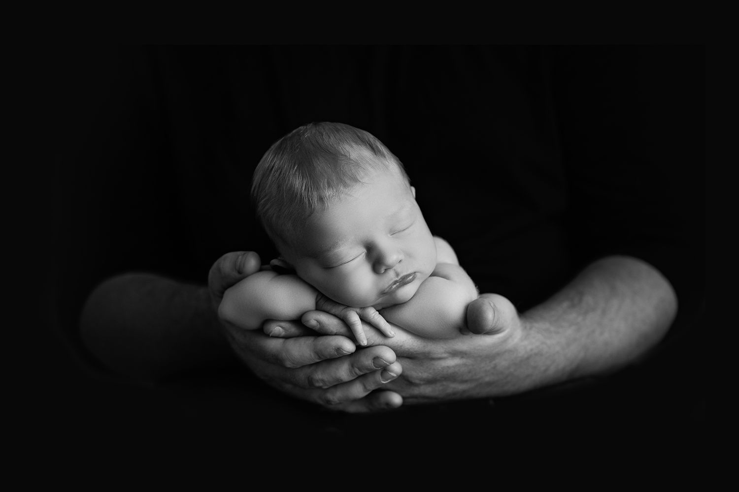 Black and white artistic portrait of hands cradling a sleeping infant.