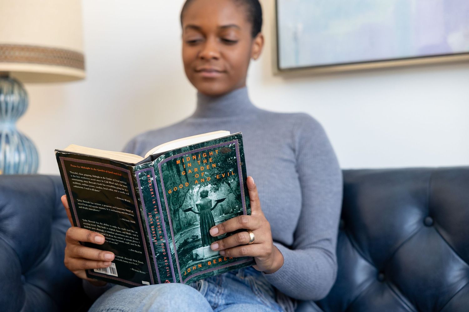 Young woman reading a fantasy novel while sitting on a leather sofa in a cozy living room.