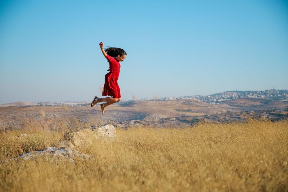 Picture of a girl in a red dress in a golden field jumping off a rock