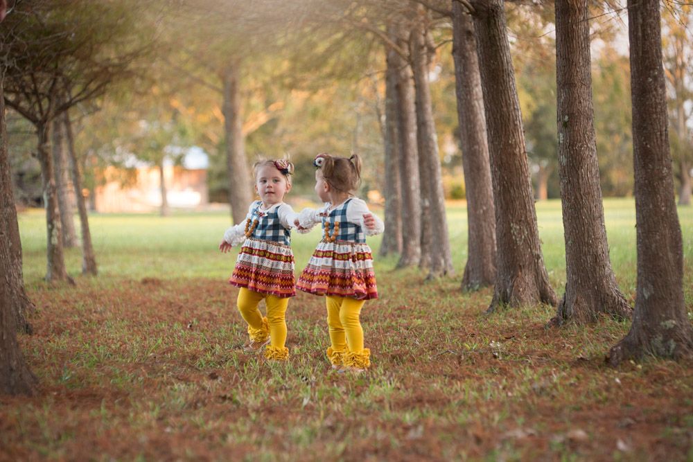 Two matching yellow rain boots walking through autumn trees in matching plaid outfits.