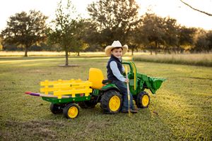 Child riding a yellow and green toy John Deere tractor in a sunny field.