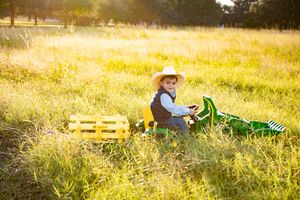 Child riding toy tractor through golden sunlit field at sunset.