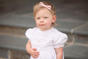Small child in white dress with pink bow wearing gentle smile.