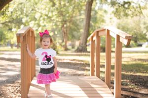 Child in pink tutu skirt walks across wooden bridge in autumn park.