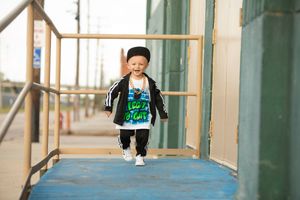A small child walks along a corridor wearing a green shirt and black jacket.