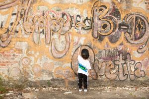 A small figure stands against a wall covered in colorful graffiti art.