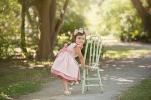 Child in pink dress playing with vintage mint green chair on tree-lined path.