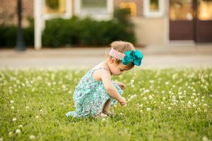 Small child in turquoise outfit picking flowers in sunny garden.