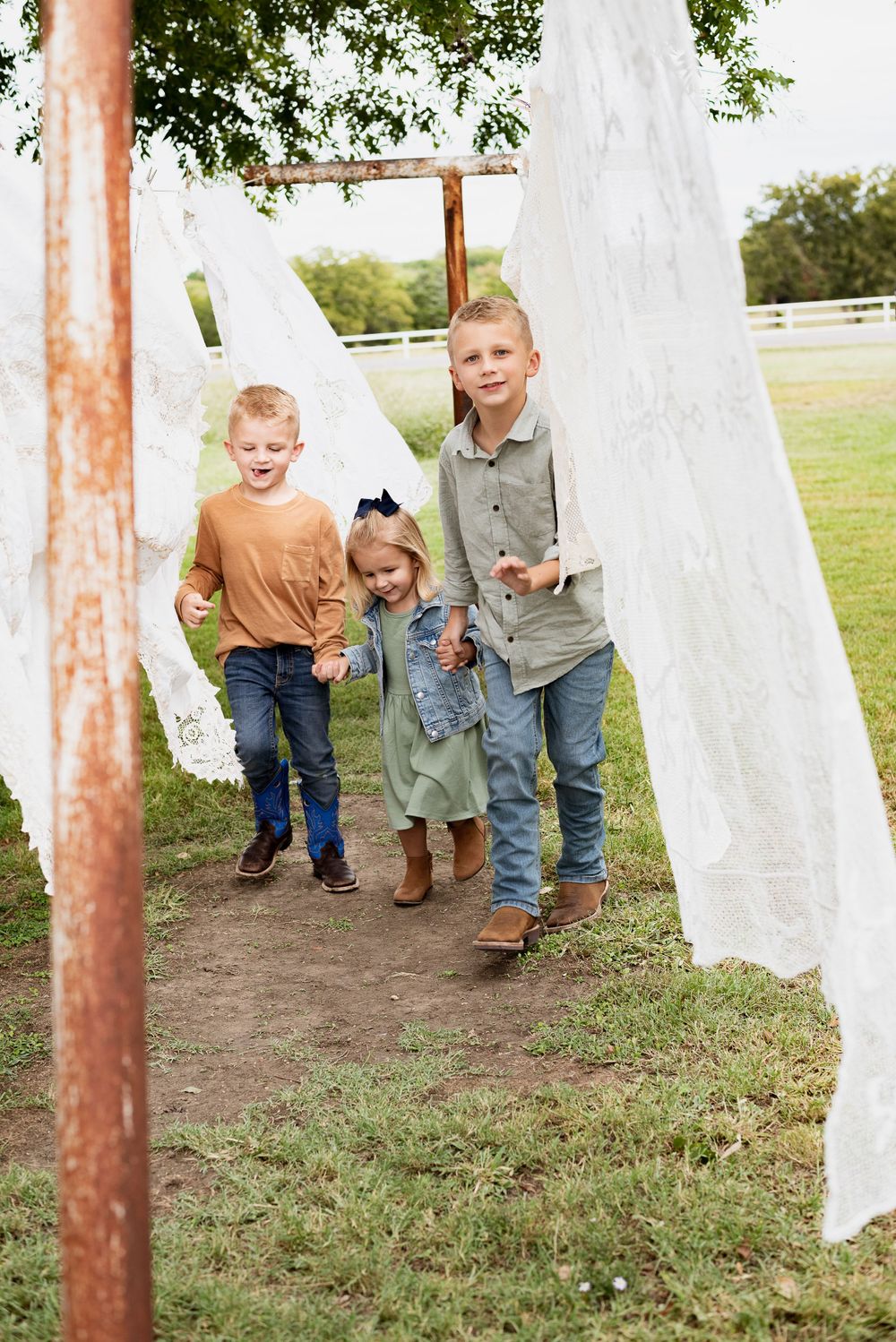 Children running and playing between white fabric panels hanging outdoors.