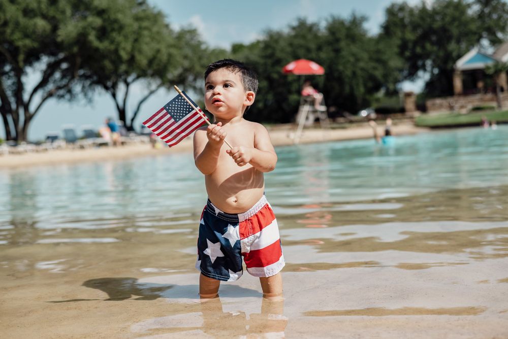 Child playing in shallow water at beach with American flag swimwear.