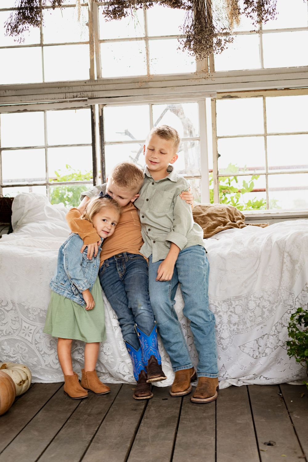 Children sitting together on wooden floor next to white lace curtains.