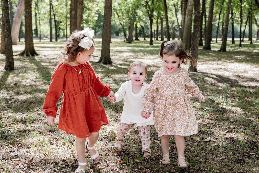 Two young children in coordinated outfits playing together in a sunlit wooded area.