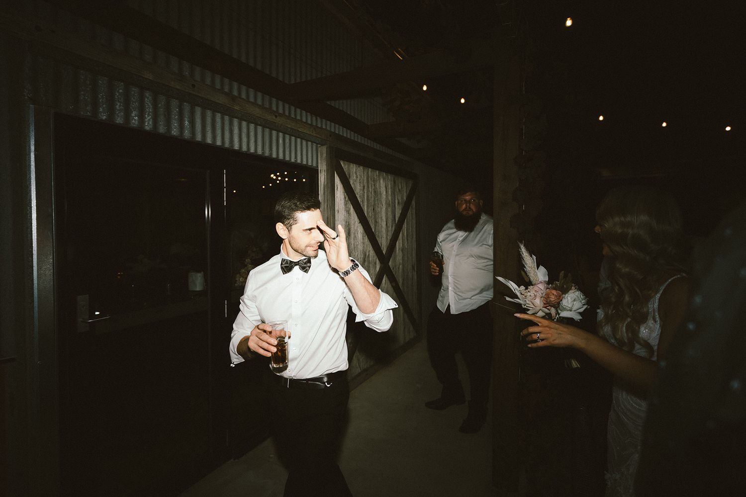 Dark reception venue with silhouettes of guests dancing and celebrating under decorative lighting.