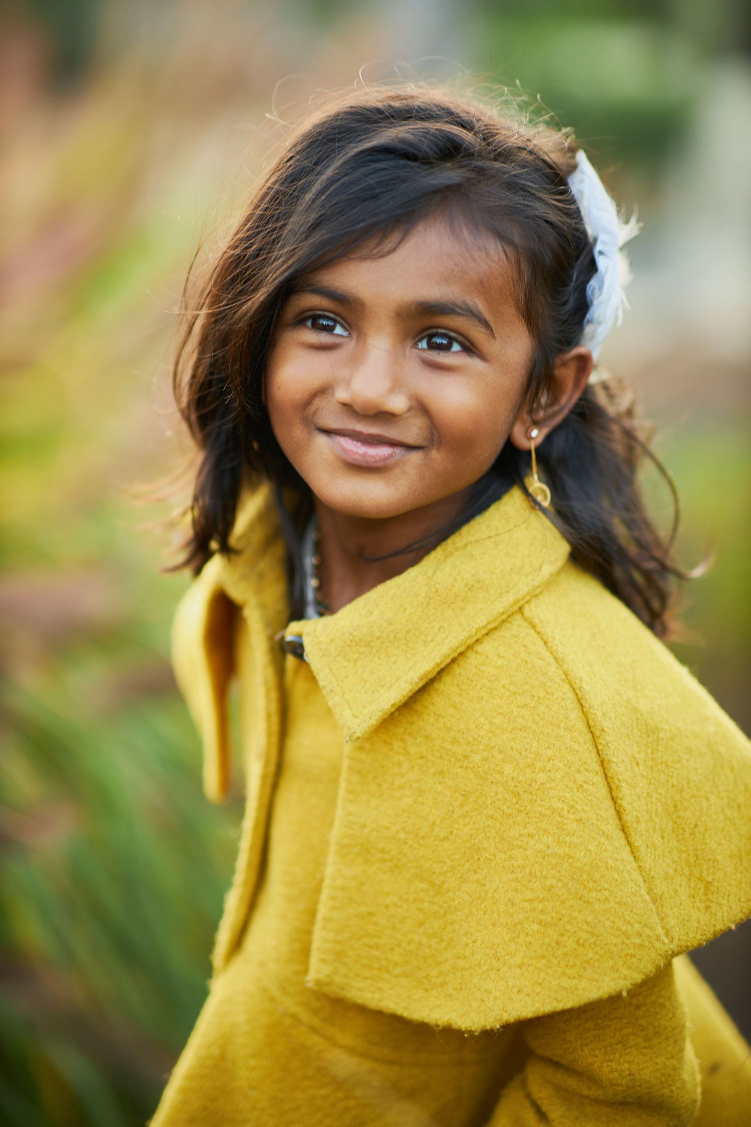 Child wearing bright yellow coat smiling against natural outdoor background.