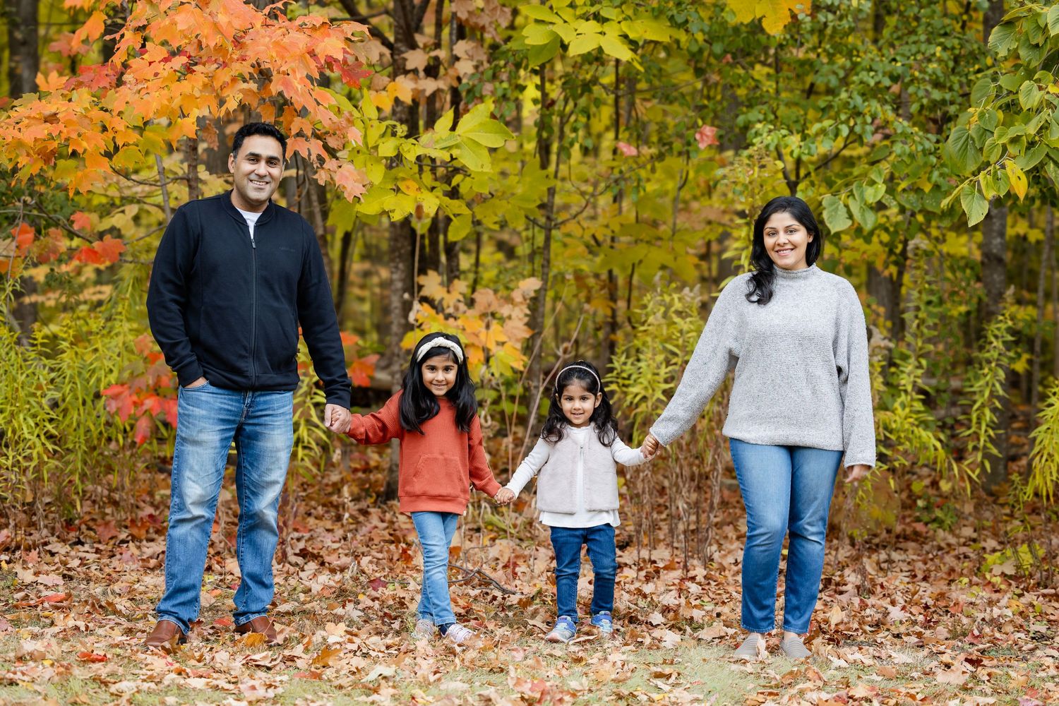 Family in casual attire standing together against backdrop of autumn foliage.