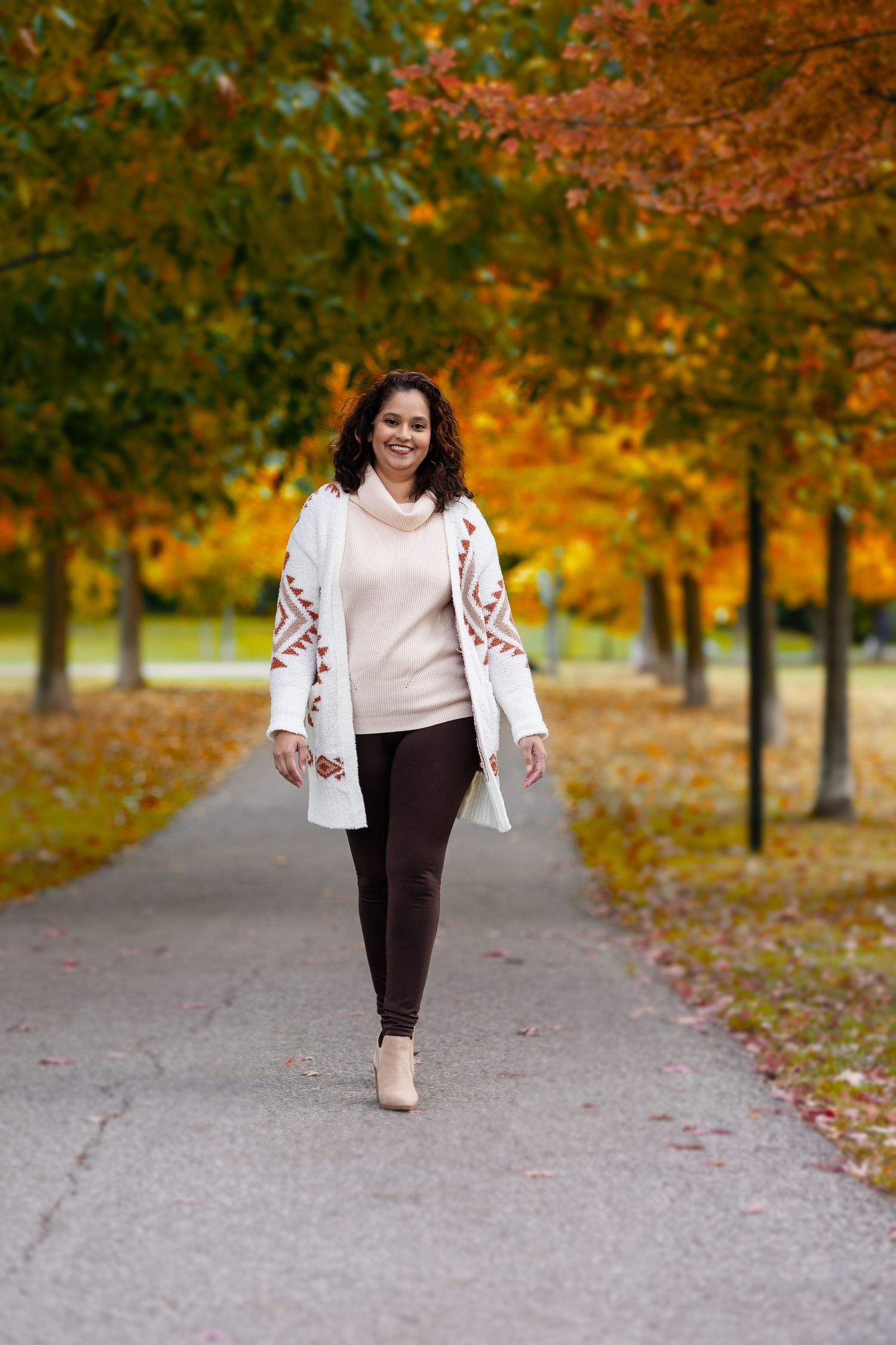 Person walks along path surrounded by vibrant autumn trees with orange and red foliage.