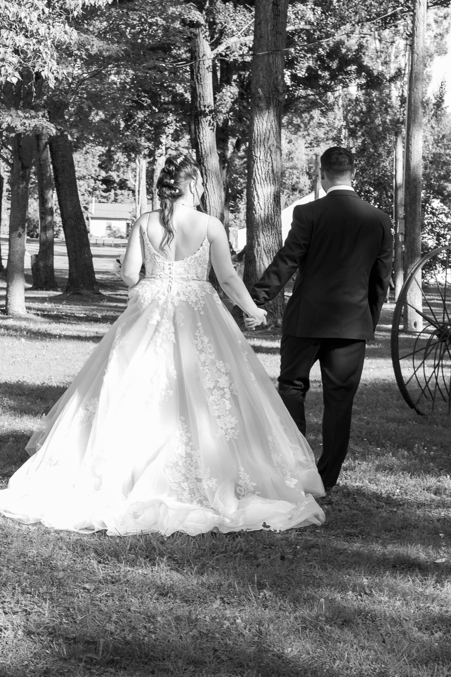Newlyweds walking through a wooded area, bride in lace wedding gown captured from behind.