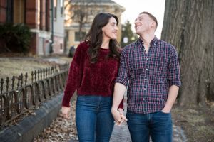 A couple walks together along a brick path near historic buildings on an autumn day.