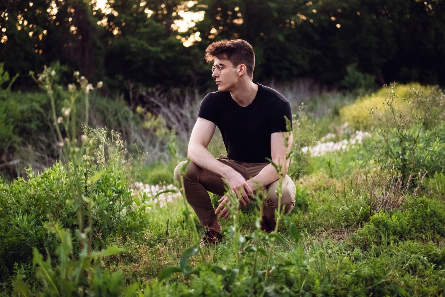 A person in black clothing sits in various poses among wildflowers during golden hour.