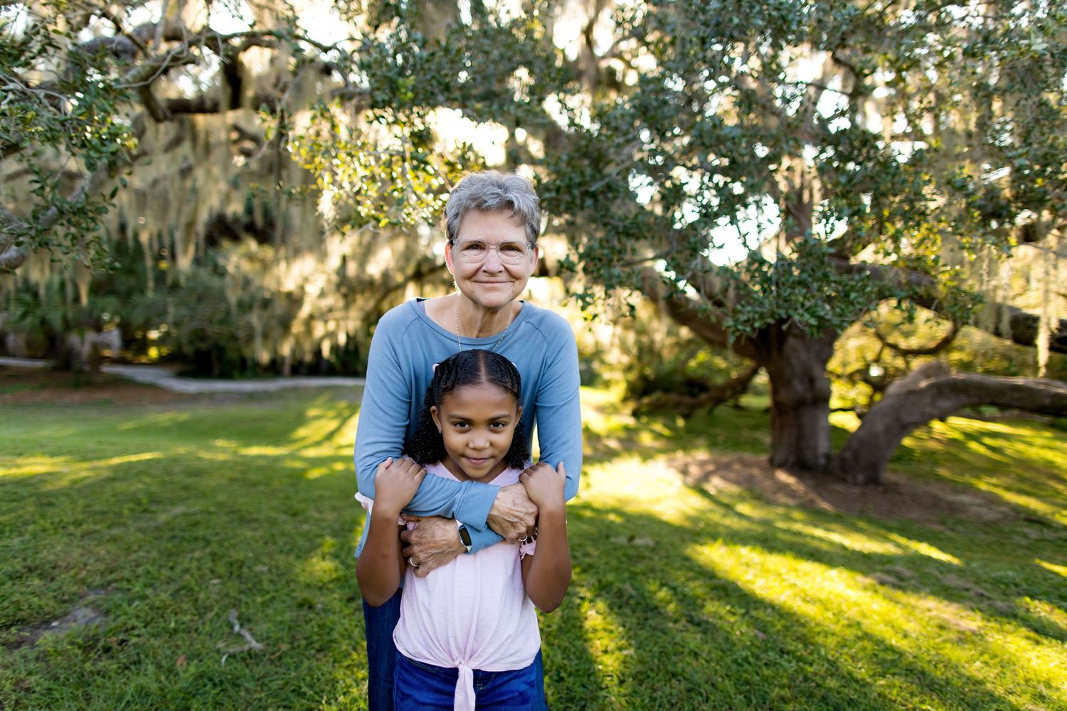 A warm embrace shared in front of moss-draped oak trees during golden hour.