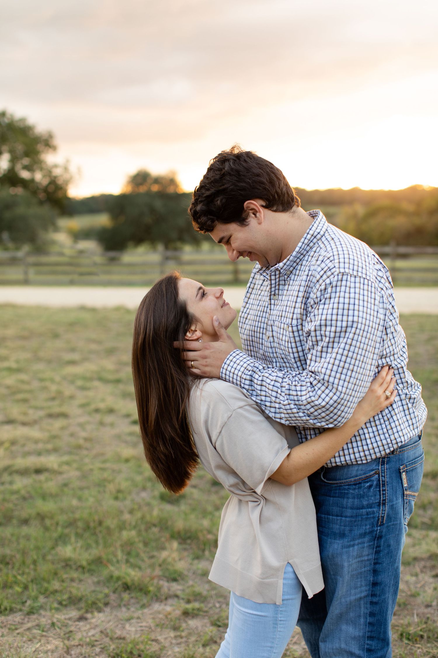 Couple embracing and sharing a tender moment in a pastoral field during sunset.