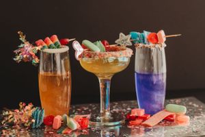 Colorful cocktails garnished with fresh fruit and herbs displayed on a dark wooden surface.