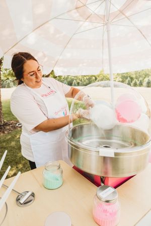 Cotton candy making process shown with a professional machine under white tent umbrellas.